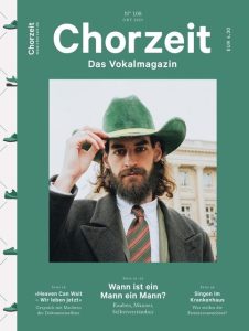 Chorzeit Nr. 108 (Oktober 2023) Eine Person in Anzug, Krawatte und grünem Hut steht vor einem historischen Gebäude und hebt die Hand zum Hut. Die Themen sind Selbstverständnis von Männern und Knaben, Singen im Krankenhaus und ein Filminterview.