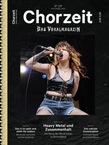 Titelbild der Zeitschrift „Chorzeit – Das Vokalmagazin“, Ausgabe Nr. 127 (November/Dezember 2025). Zu sehen ist eine Sängerin auf einer Bühne mit Mikrofon in der Hand, gekleidet in ein schwarzes Oberteil und Jeansshorts. Im Hintergrund sind Bühnenlichter sichtbar. Auf dem Cover stehen Themen wie „Heavy Metal und Zusammenhalt“, „Das A ist gelb und steht für anders“ und „Das sakrale Grammophon“.