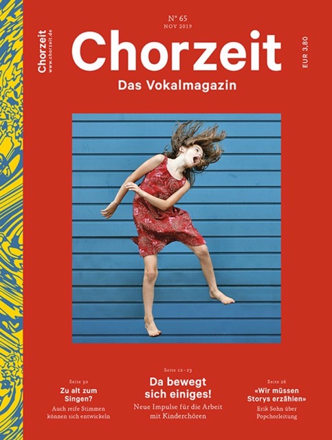 Chorzeit Nr. 65 (November 2019) Cover mit rotem Hintergrund: Ein Mädchen in einem roten Kleid springt vor einer blauen, gestreiften Wand. Die Themen sind Entwicklung reifer Stimmen, Kinderchöre und die Bedeutung von Storytelling.