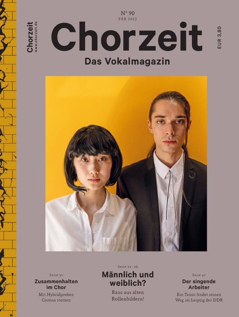 Chorzeit Nr. 90 (Februar 2022) Zwei Menschen stehen nebeneinander vor einer gelben Wand, beide in weißem Hemd und dunklem Sakko. Die Themen sind Geschlechterrollen, Zusammenhalt im Chor und Sängerbiografien.