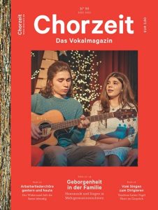 Chorzeit Nr. 99 (Dezember 2022) Zwei Menschen sitzen auf einer Bühne vor Lichterketten, einer spielt Gitarre. Die Themen sind Familienmusik, Arbeiterliederchöre und Chorleiterporträts.