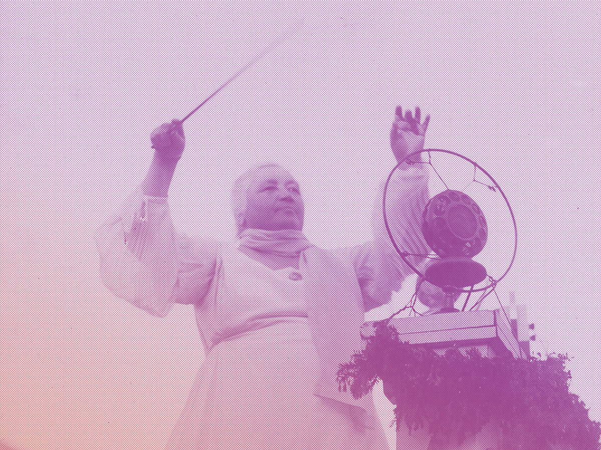 Ein schwarz-weiß-Foto einer Frau, die dirigiert. In einer Hand hält sie einen Taktstock, die Körperspannung ist groß. Sie steht auf einem Podest vor einem Mikrofon aus den 1920er Jahren.