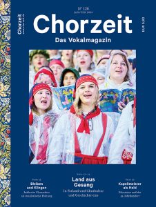 Chorzeit Nr. 128 (Januar 2026) Eine Gruppe von Sängerinnen und Sängern in traditionellen estnischen Trachten steht dicht beieinander und hält Liederbücher. Die Kleidung ist weiß mit roten Bändern und Kopftüchern, einige tragen durchsichtige Regencapes. Die Szene vermittelt Gemeinschaft und kulturelle Verbundenheit beim Chorgesang im Freien.