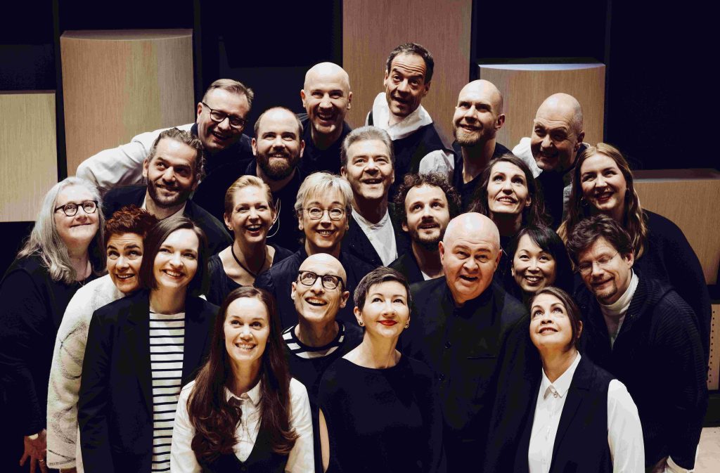 Das SWR Vokalensemble lachend vor runden Holzsäulen