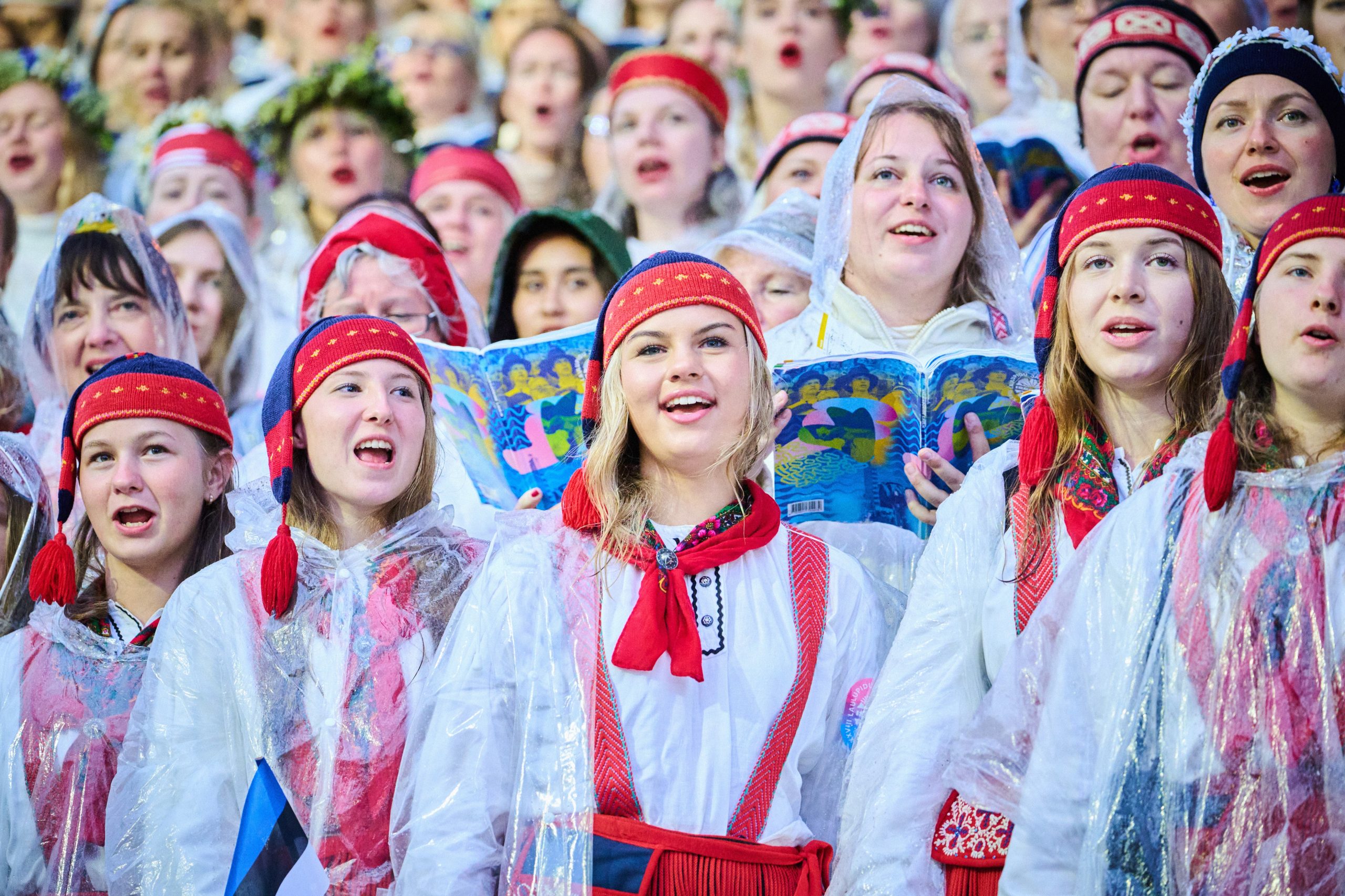 Eine Gruppe Frauen in estnischen Trachten in rot und weiß steht in einer Gruppe zusammen. Sie singen.