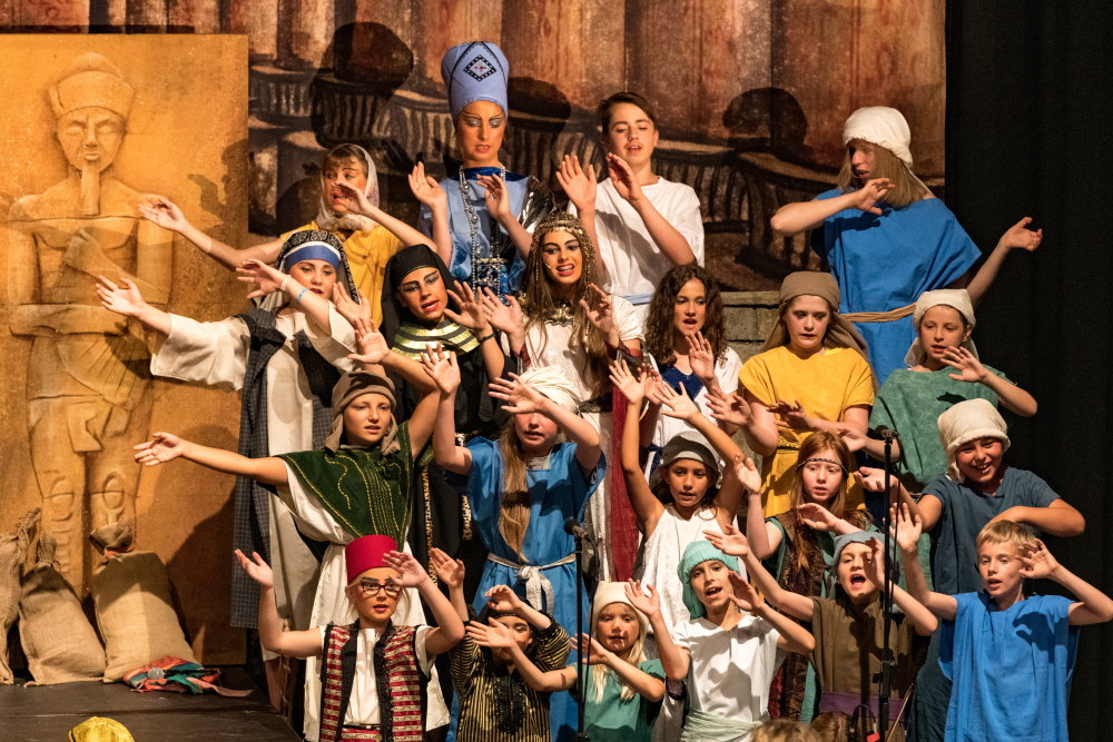 Ein Kinderchor in Kulissen des Alten Agypten singt und winkt mit den Händen.