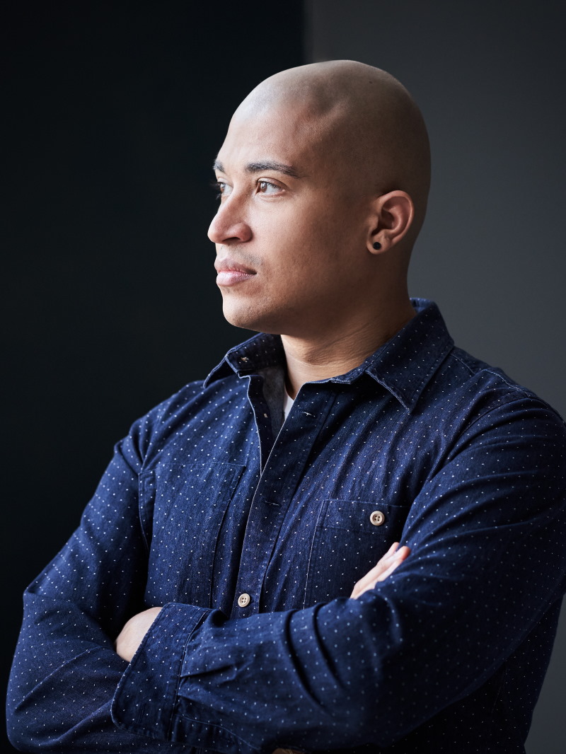 Der Komponist Daniel Kidane in blauem Hemd vor dunkler Wand