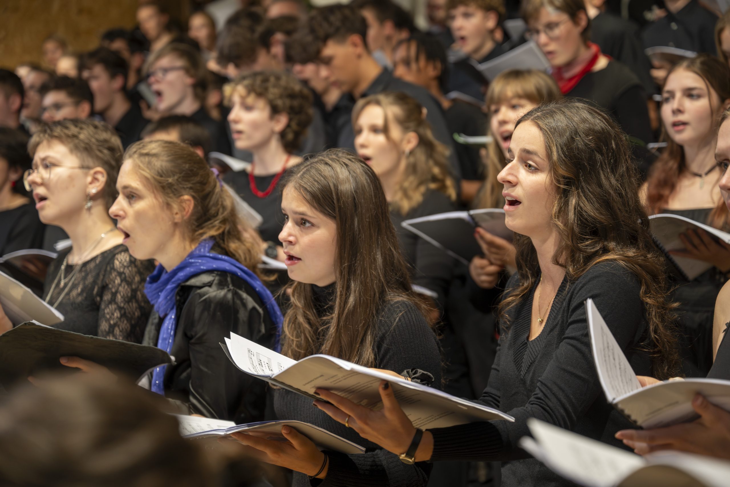 Ein Blick in den singende Chor. Mehrere Sängerinnen und Sänger stehen dicht beieinander mit Noten in der Hand.
