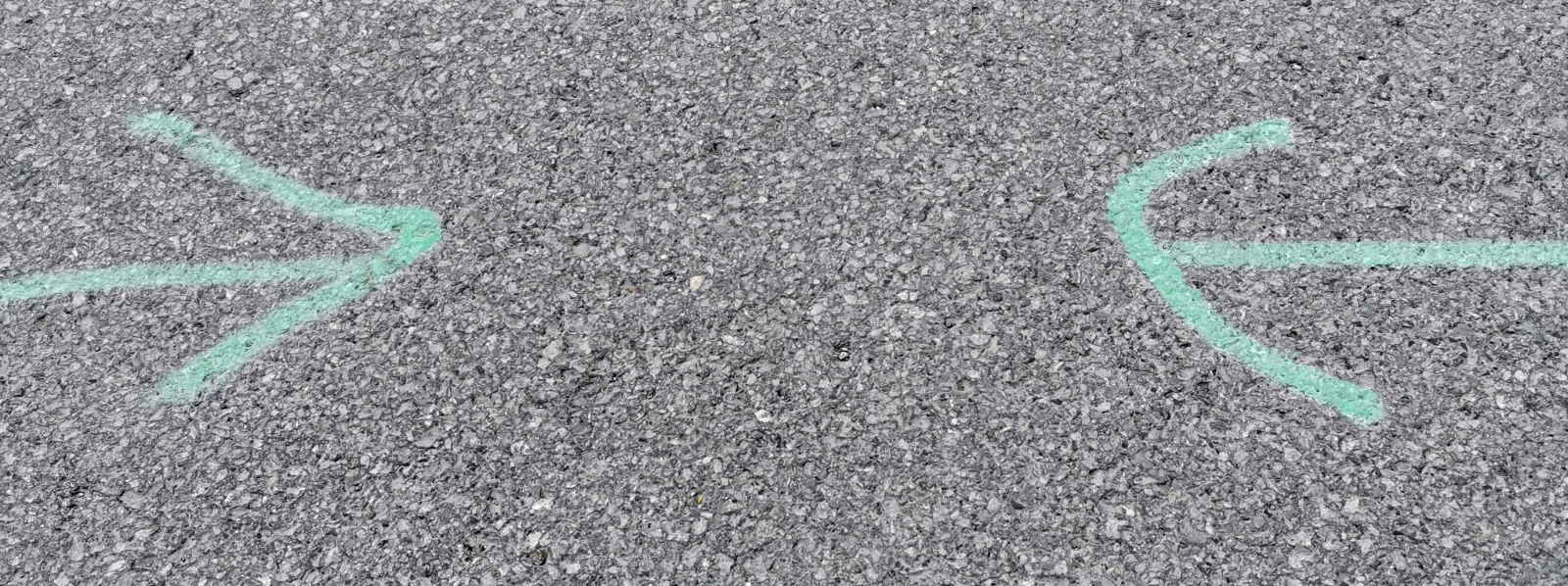Auf einer grauen Asphaltfläche sind mit grüner Kreide zwei Pfeile gezeichnet, die aufeinander zeigen.