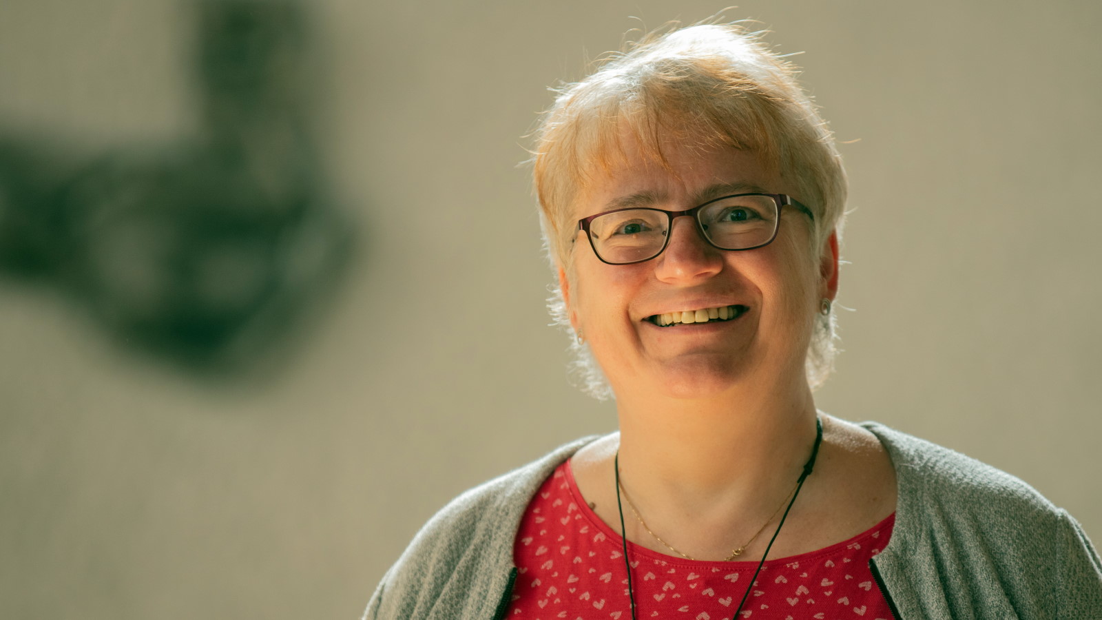 Die Kirchenmusikerin und Chorleiterin Jutta Michel-Becher, mit schwarzer Brille, rotem Oberteil und heller Jacke, lächelt entspannt.