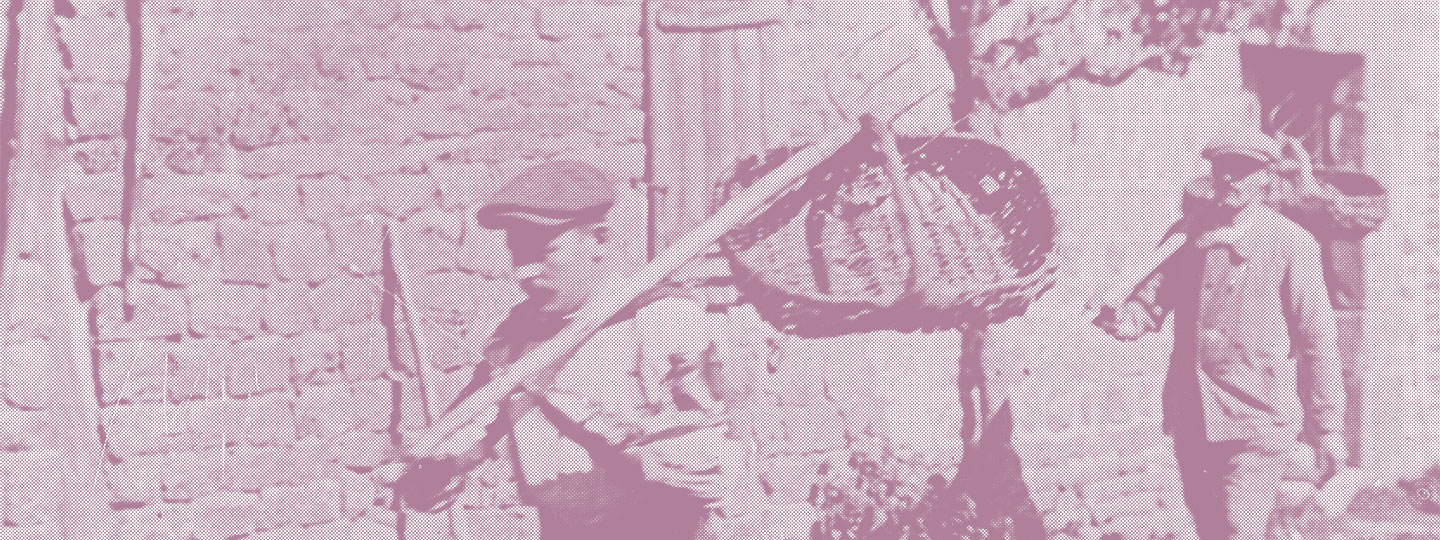 Zwei Männer in altertümlicher Kleidung und mit Schiebermütze tragen jeweils einen Korb, den sie mit einer über die Schulter getragenen Heugabel halten.